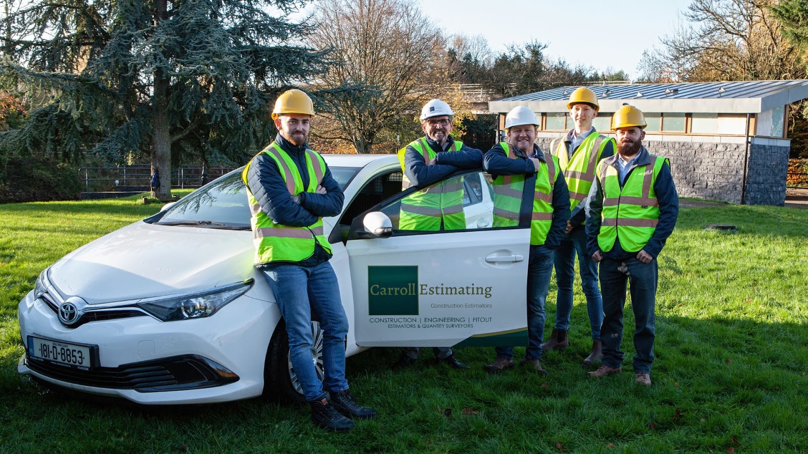 Carroll Estimating team standing beside a car with company logo.