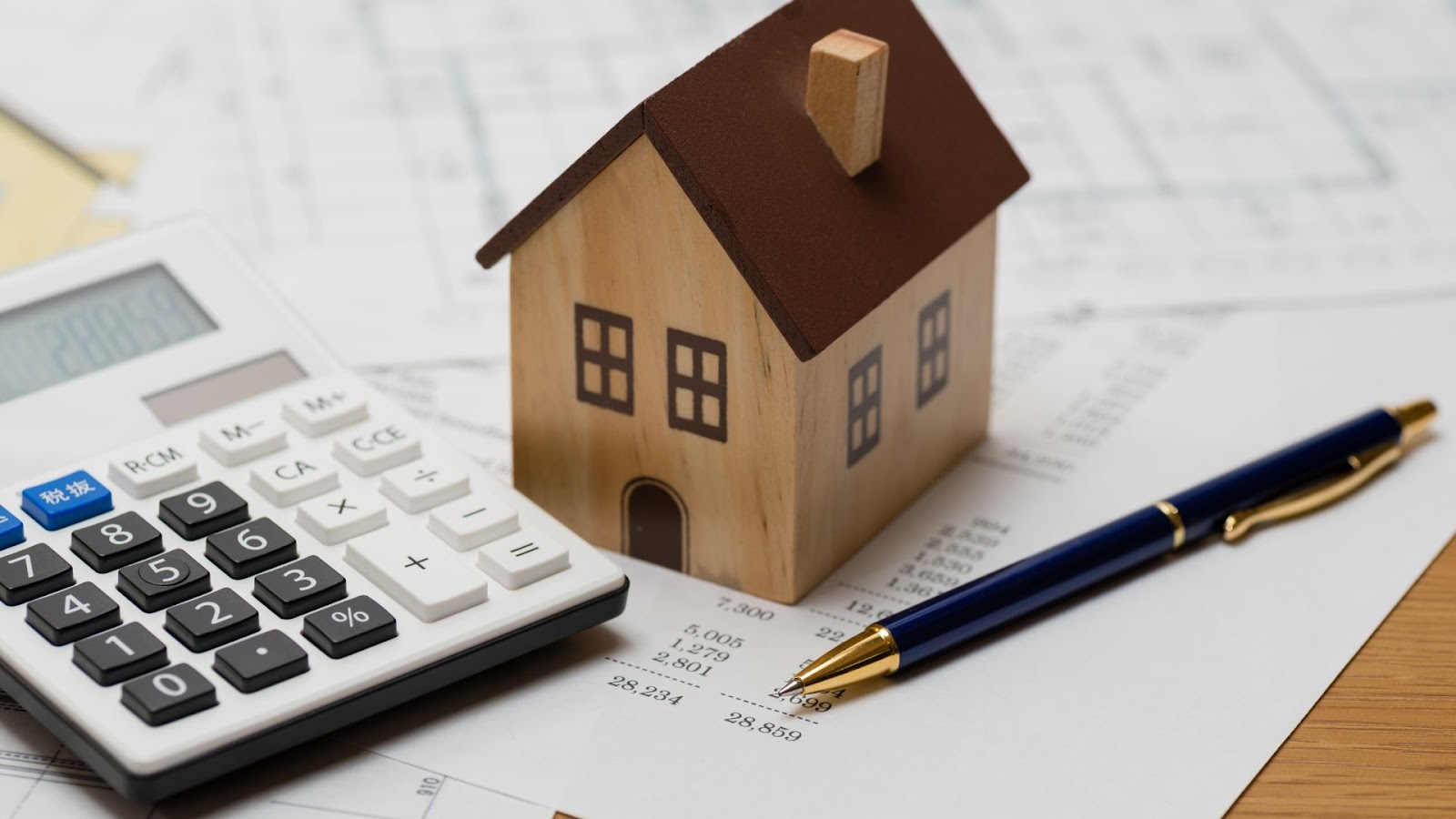 Calculator, a house model, and a pen on top of a piece of paper