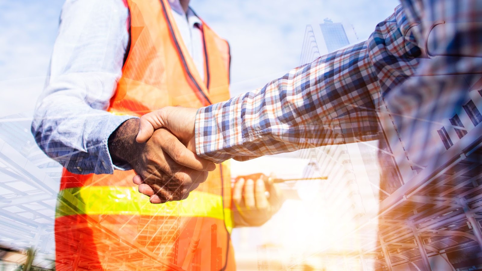 Two construction workers shaking hands in front of a building