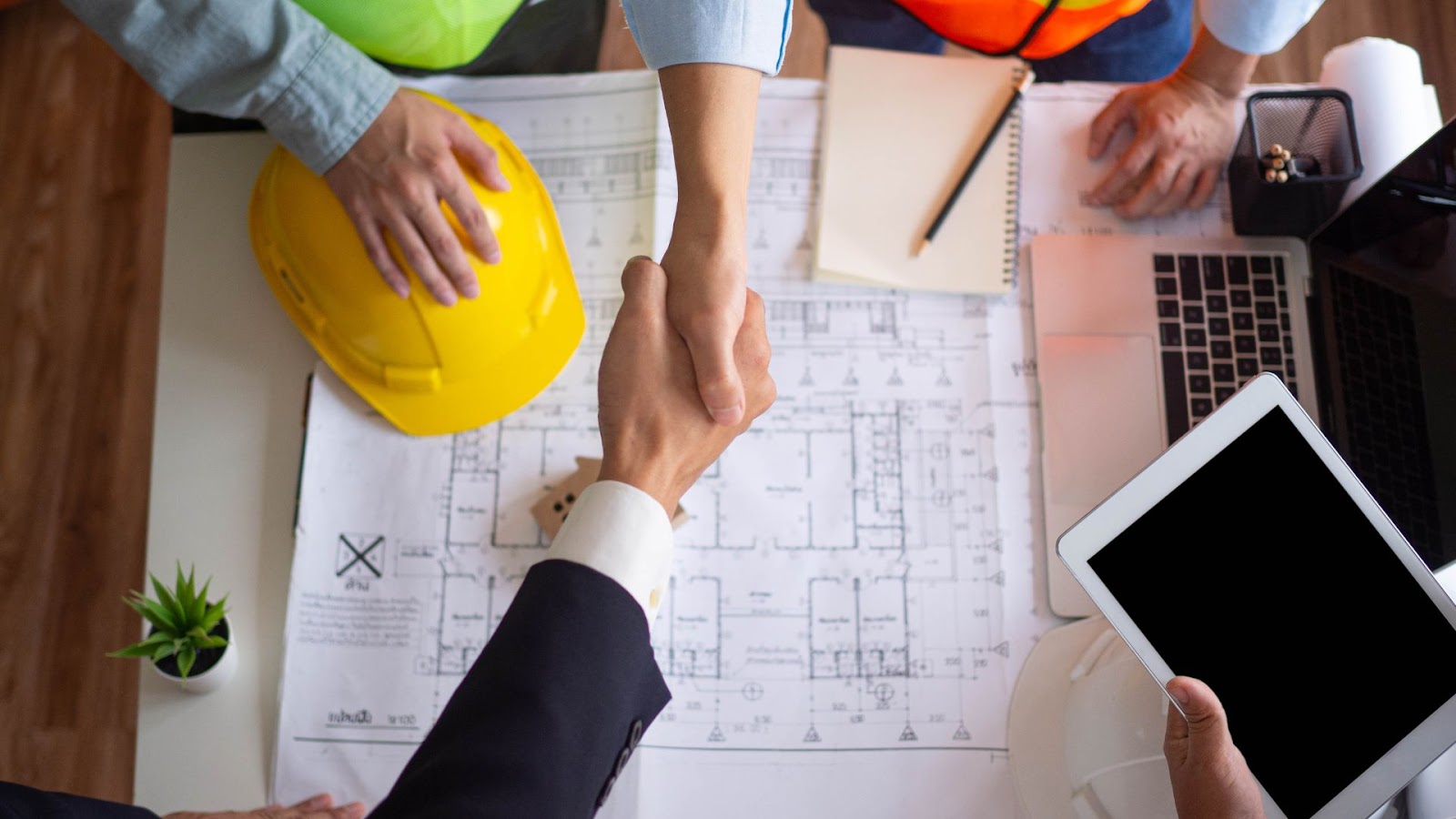 Group of people shaking hands at a table with construction plans
