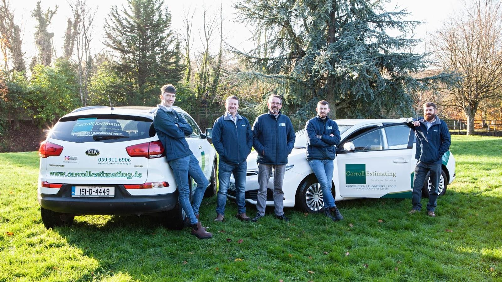 Carroll Estimating team standing beside cars with company logo. 