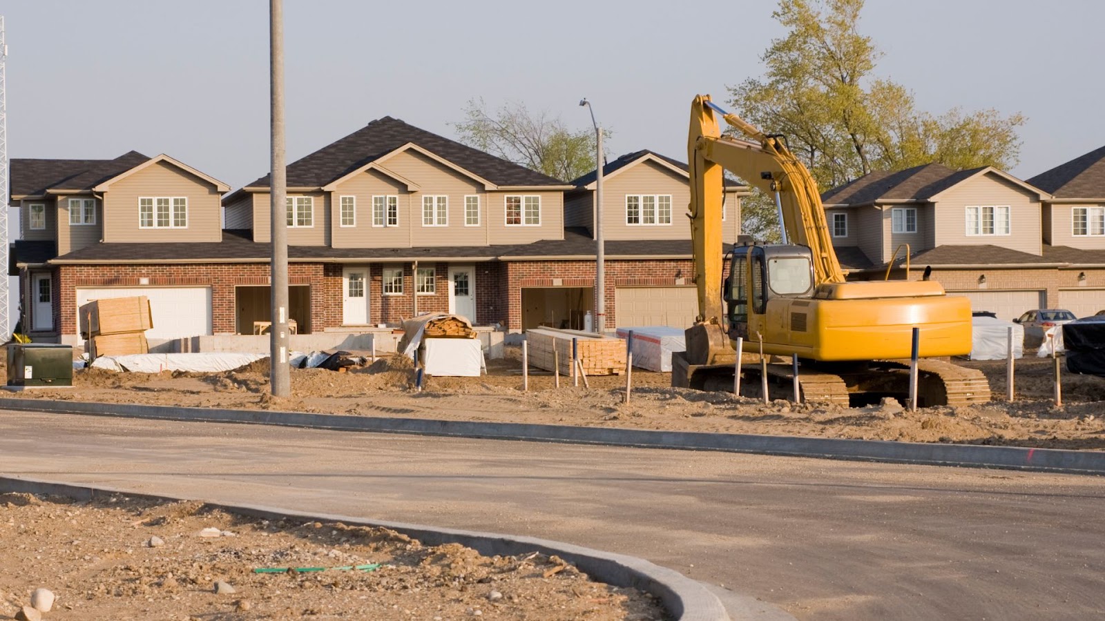 Construction site with a yellow excavator in the middle of a residential neighborhood