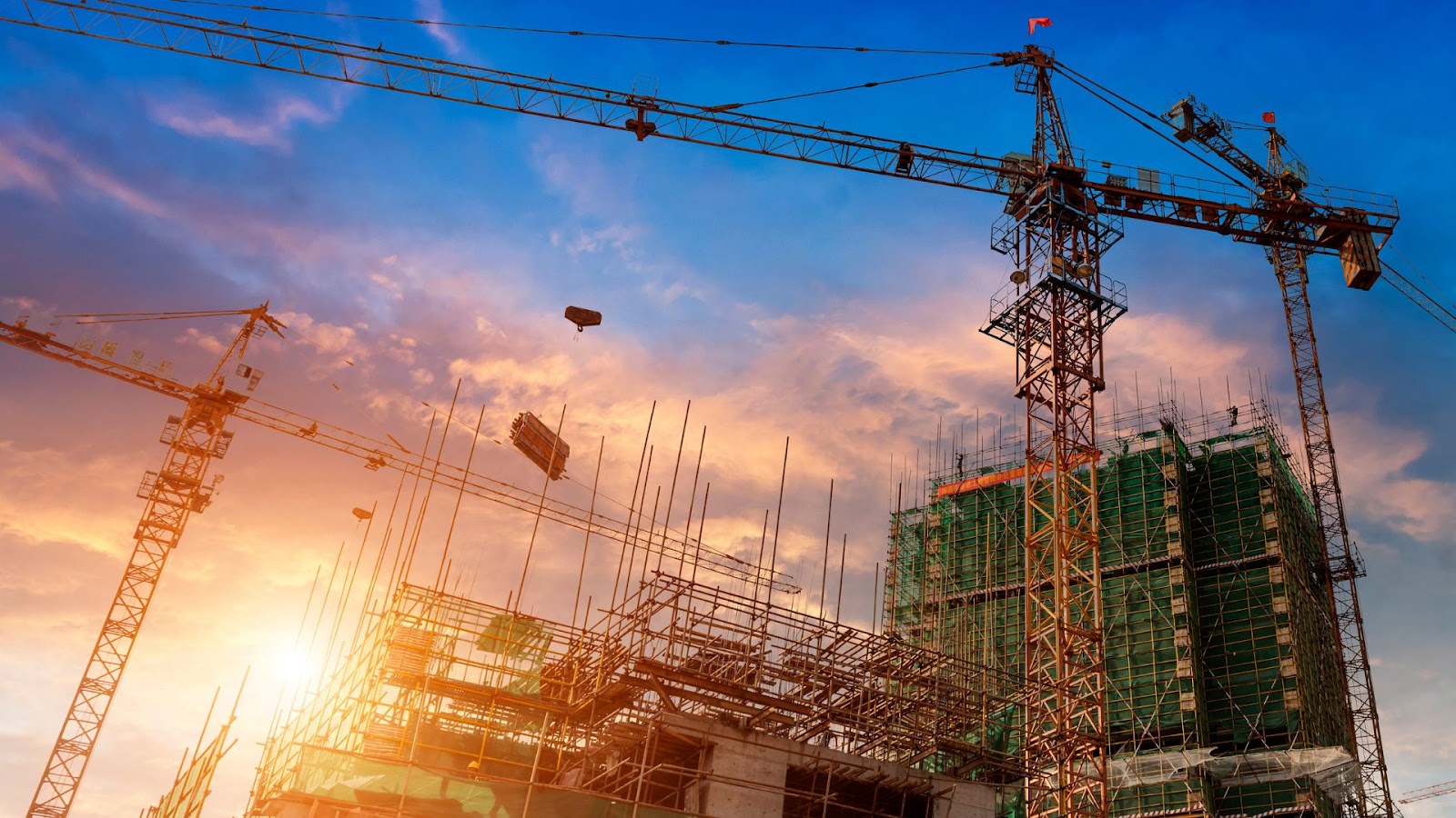 Construction cranes in front of a building under construction.