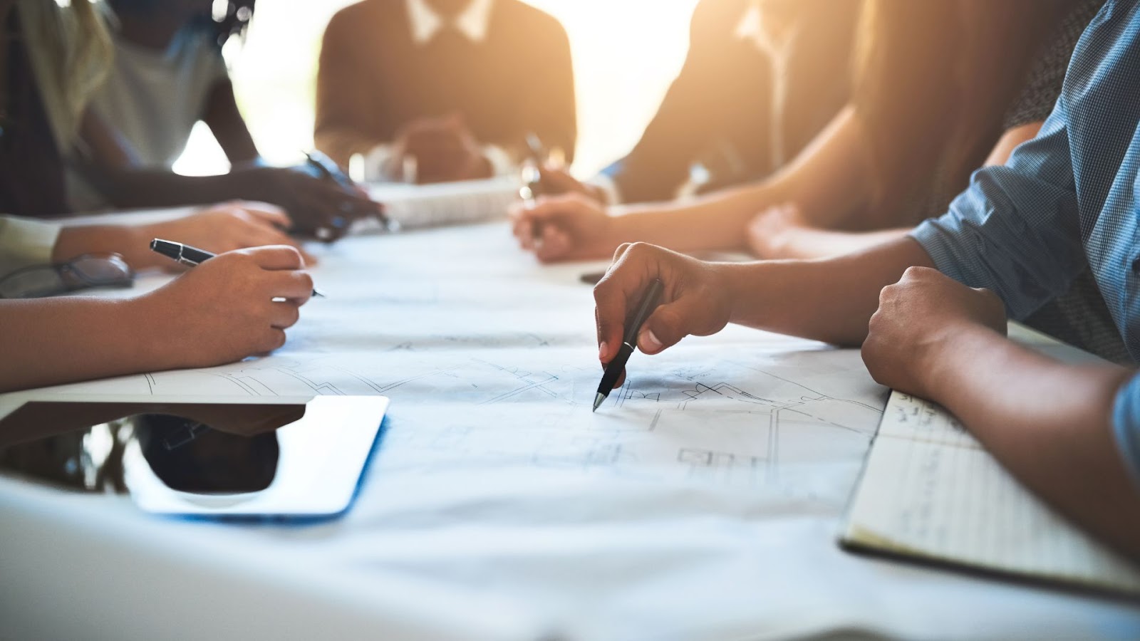 Group of people sitting around a table with a pen and paper.