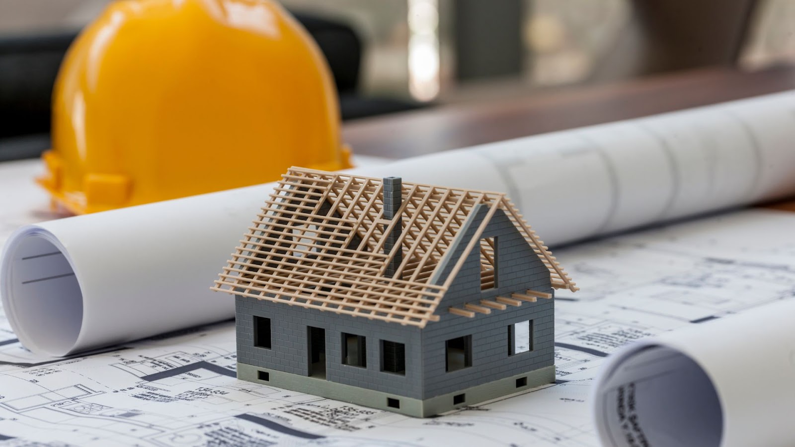 A model of a house sits on top of blueprints and a hard hat.