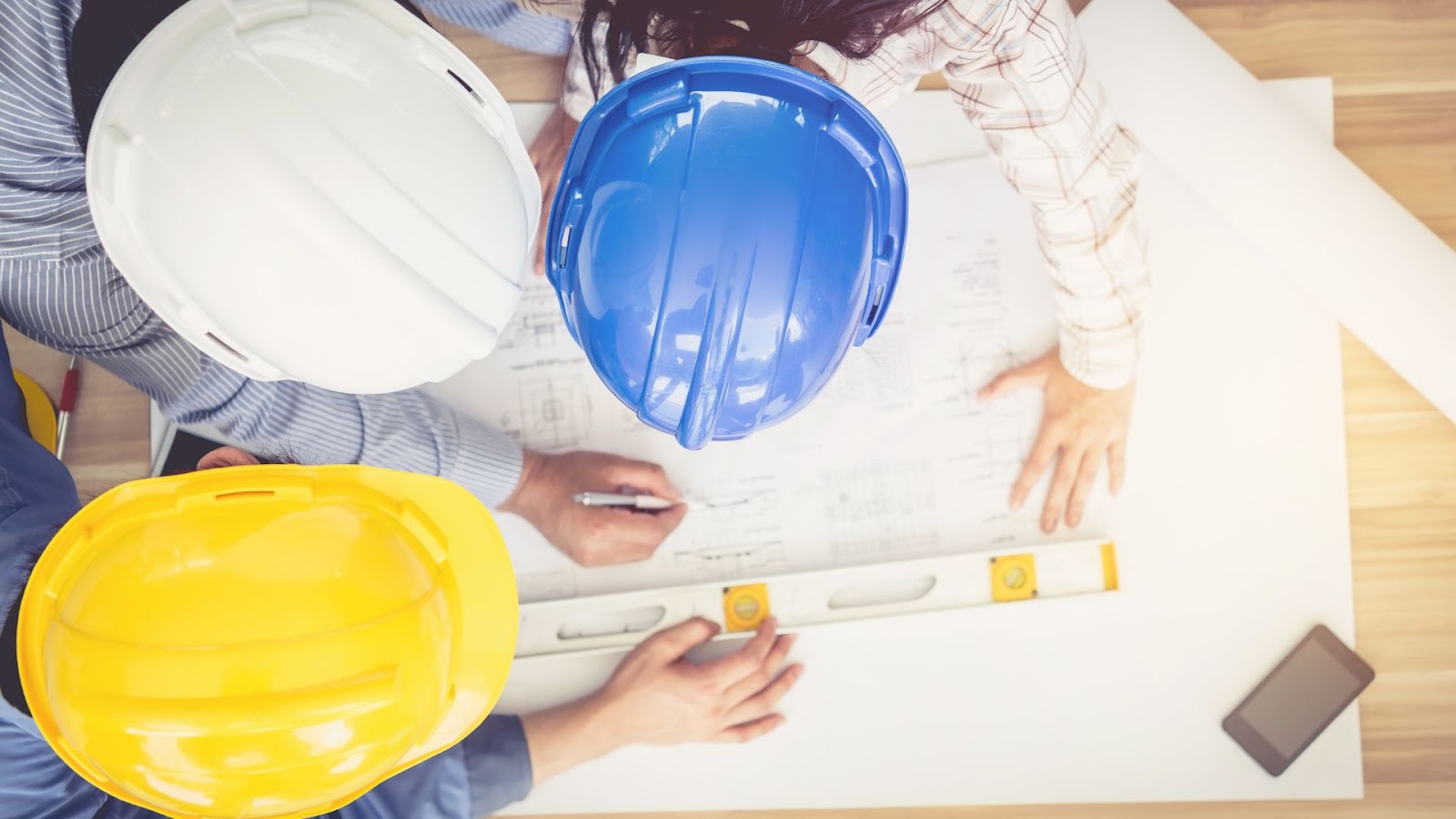 Three people in hard hats looking at blueprints.