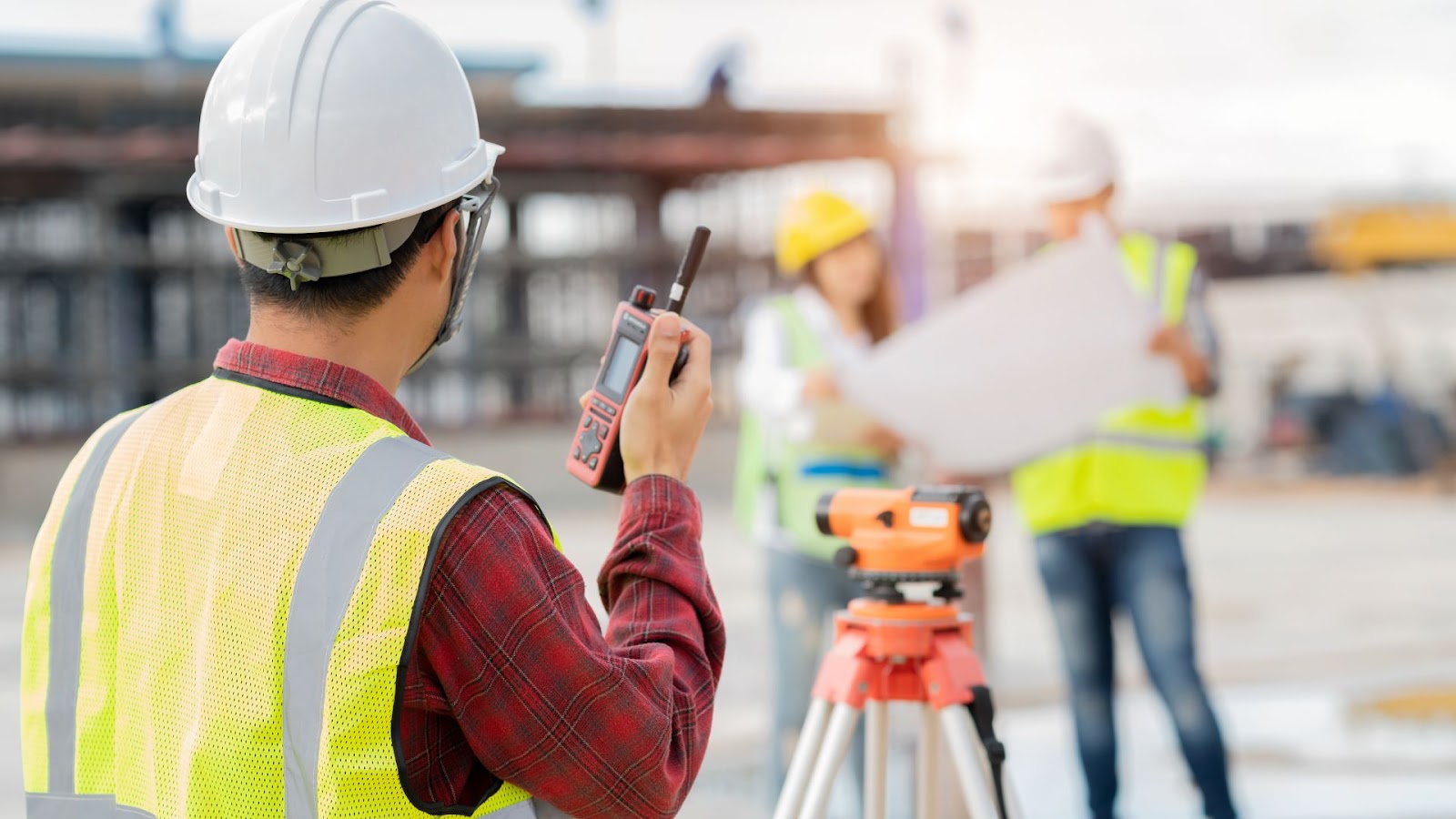 A person in a hard hat and safety vest stands beside a construction site.