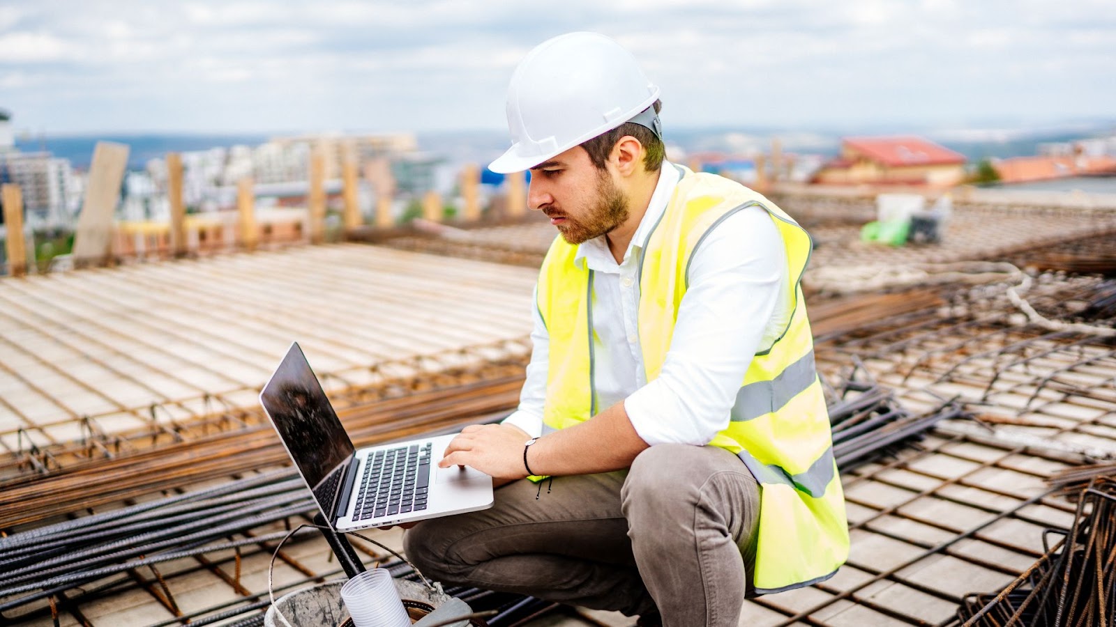 Person in a hard hat and safety vest using a laptop on a construction site